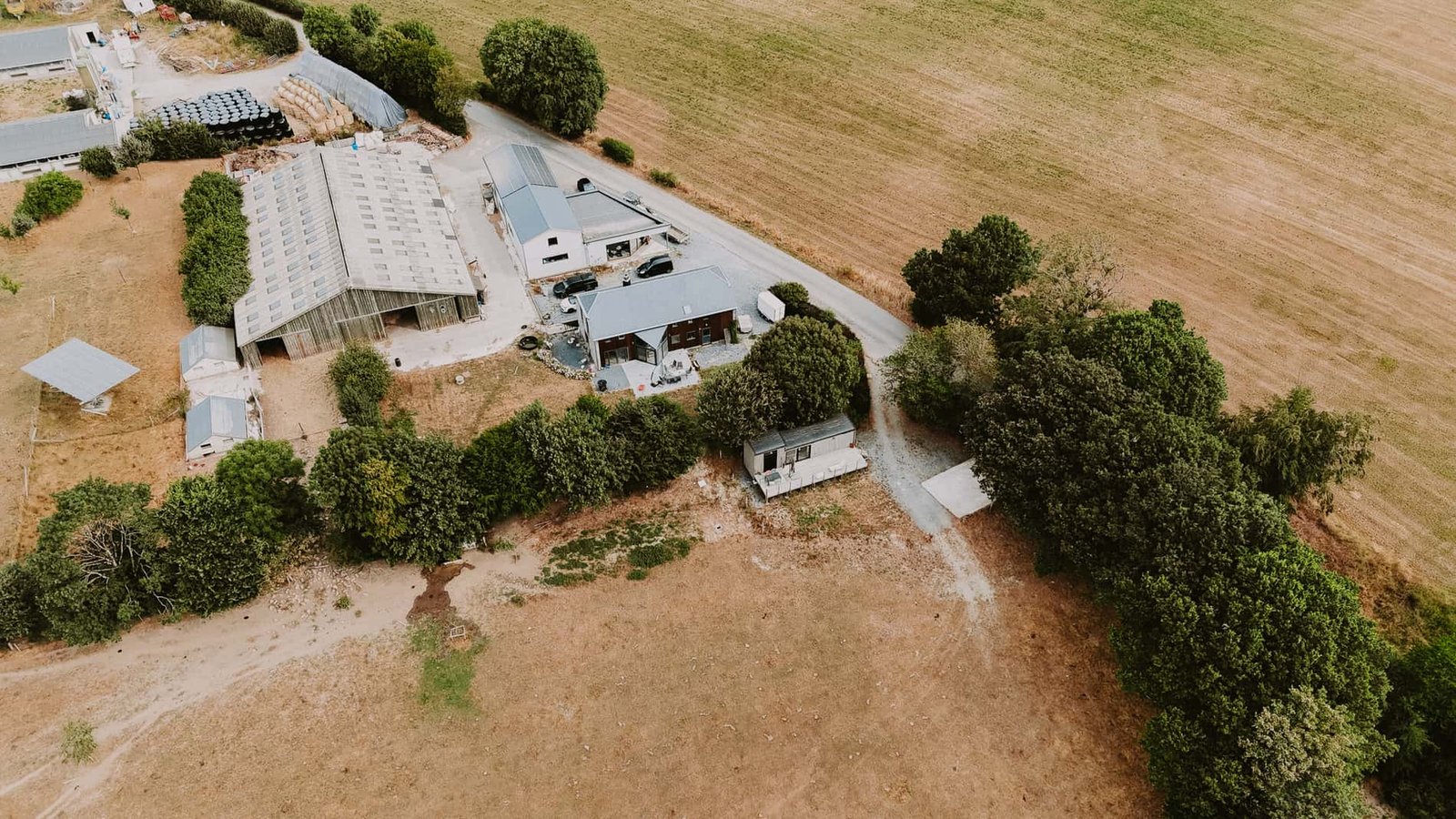Vue aérienne éloignée de la Tiny House d'Habaru et de la ferme, nichées entre champs et forêts de l'Ardenne belge